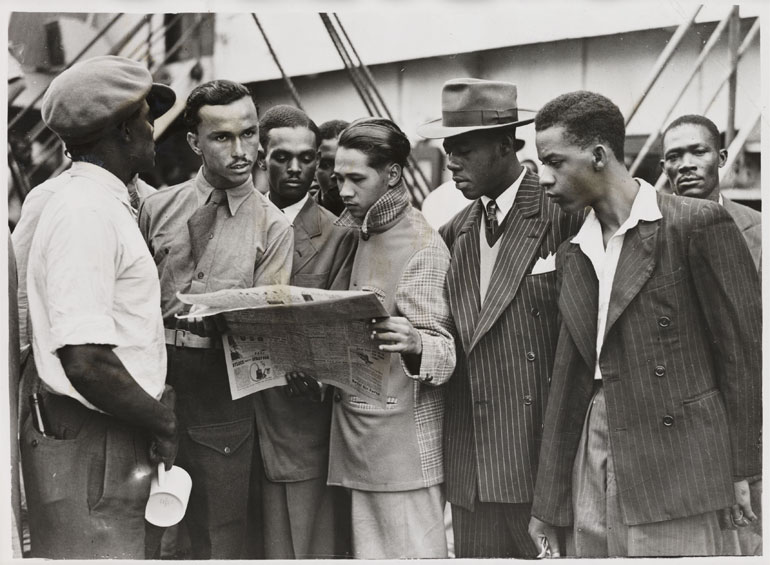 Passengers on the Windrush reading a newspaper as they wait to disembark.